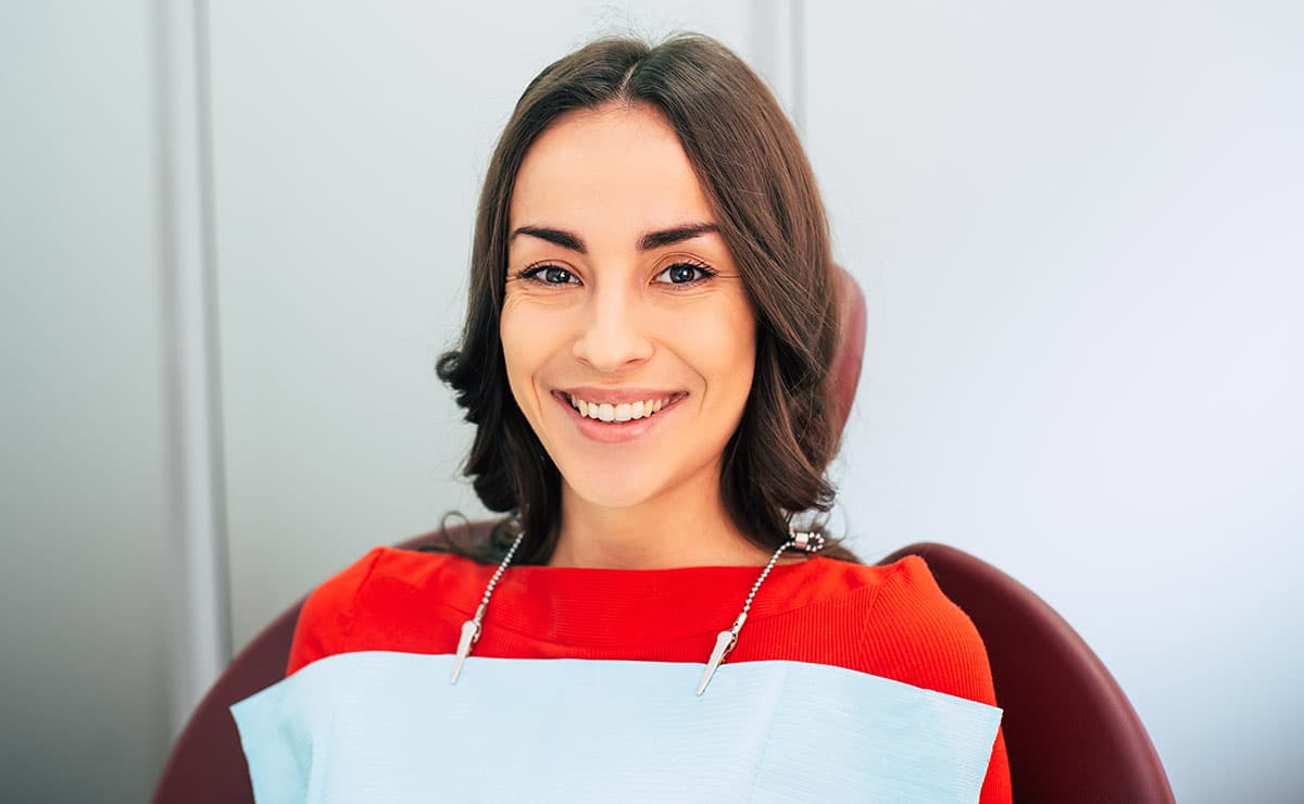 Young woman smiling in dental chair with bib during cleaning appointment at Esthetique Dentistry Ashburn