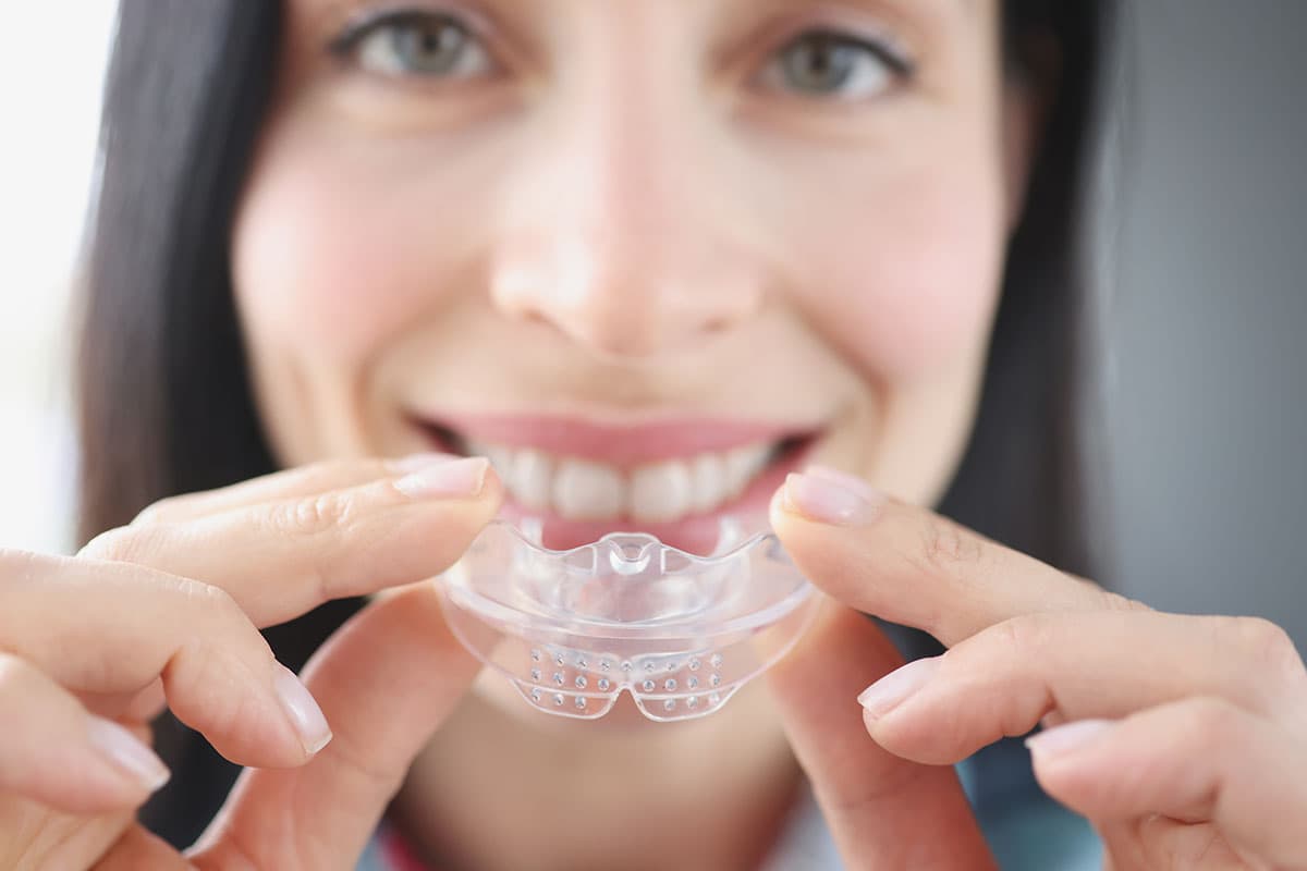 Woman holding a custom clear occlusal guard at Esthetique Dentistry Ashburn