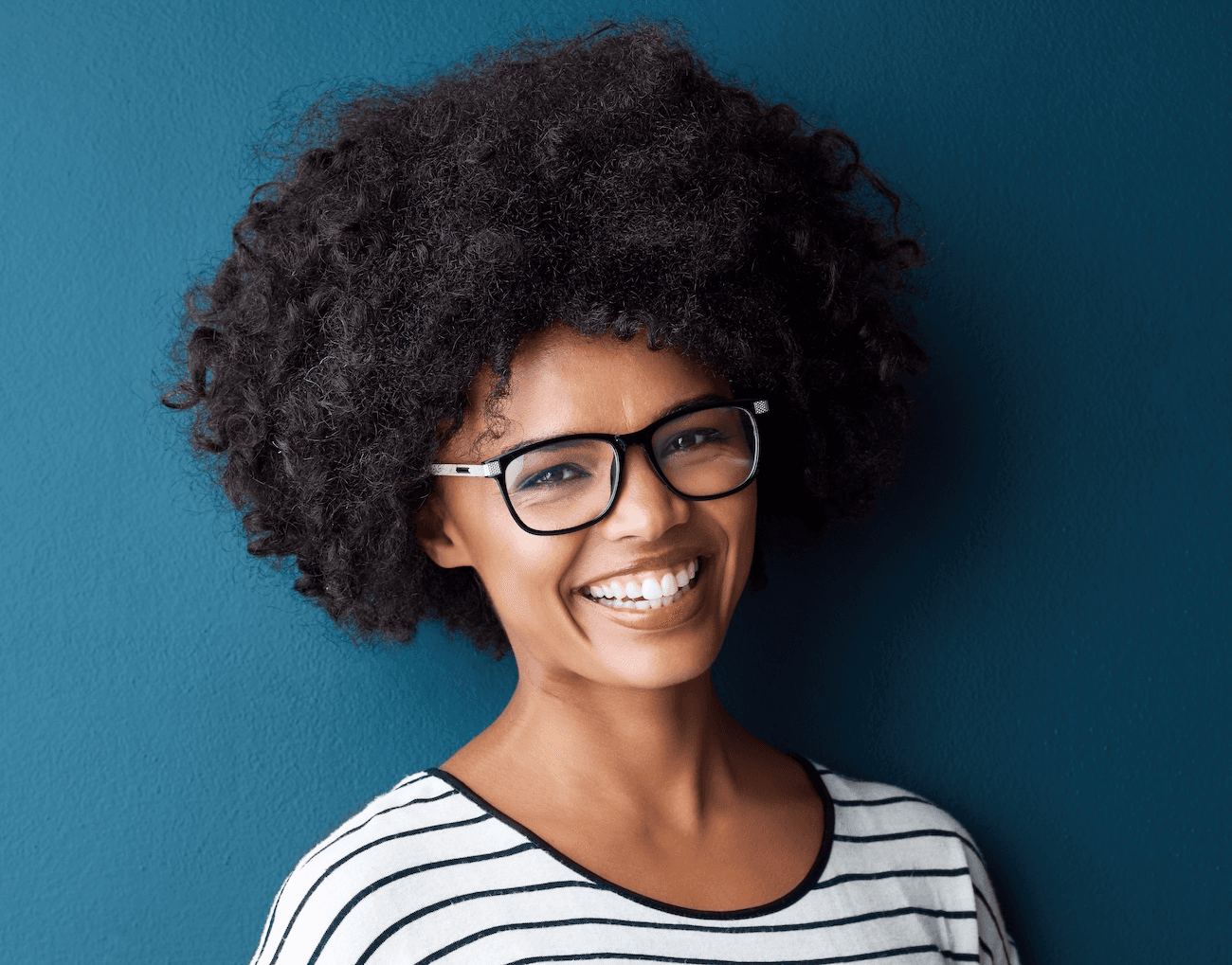Young woman with natural hair and glasses smiling brightly after teeth whitening at Esthetique Dentistry Ashburn